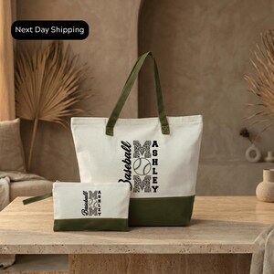 A white tote bag with a green trim and a smaller white bag with a similar design are displayed on a wooden table.