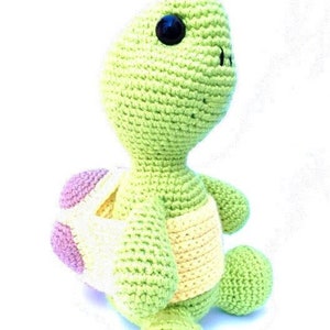 May include: A crocheted green turtle toy with a yellow and pink shell. The turtle has a black button eye.