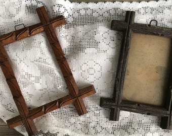 Könnte beinhalten: Zwei Vintage-Holzbilderrahmen. Einer ist mittelbraun mit geschnitzten Details, der andere dunkler braun. Beide Rahmen haben eine rechteckige Form und ein kreuzartiges Design. Sie werden auf einem weißen Spitzentuch präsentiert.