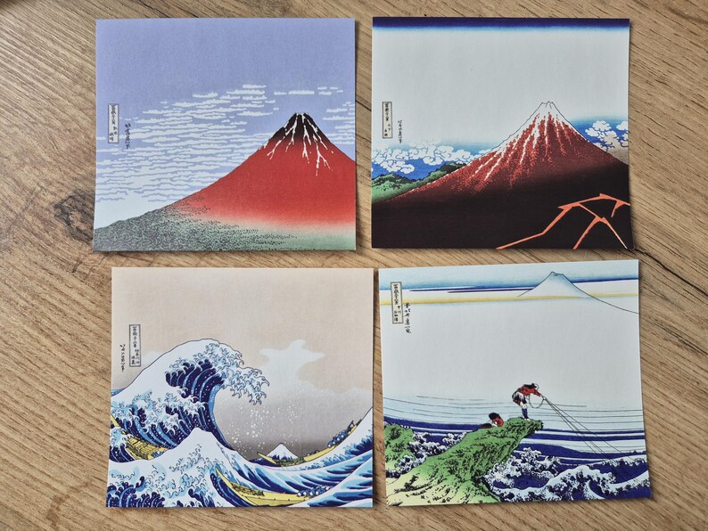 May include: Four square art prints featuring Japanese landscape scenes. The prints depict Mount Fuji, a large ocean wave, and figures fishing. Each print has a unique color palette, including red, blue, and beige.