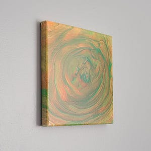 May include: Abstract painting on canvas with swirling green and orange colors. The painting has a circular pattern with a dark center.