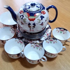 Könnte beinhalten: Ein Vintage-Tee-Set mit einem blauen und weißen Blumenmuster. Das Set enthält eine Teekanne, eine Zuckerdose, eine Milchkännchen und sechs Teetassen und Untertassen.