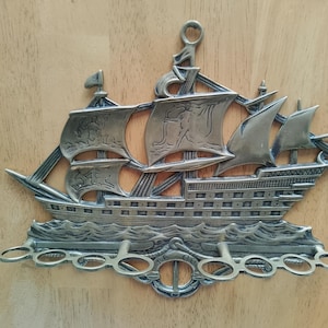 Peut inclure: Décoration murale en métal argenté en forme de voilier. Le navire présente des voiles détaillées, un gréement et un motif de vagues décoratives en bas. Il comporte des supports en forme de trou de serrure et une boucle en haut pour l'accrocher.