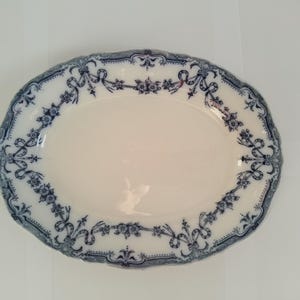 May include: A white oval serving platter with a blue and white floral design. The design features a repeating pattern of bows and flowers.