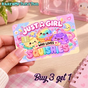 May include: A rectangular card featuring a pastel-colored graphic with the text JUST A GIRL WHO LOVES SQUISHIES. The design includes a rainbow ice cream cone, a purple jelly cube, and a yellow block with a chip, all with smiling faces.