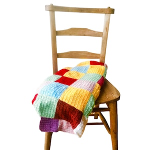 May include: A wooden chair with a colourful patchwork blanket draped over it. The blanket is made of different coloured squares of yarn, including red, yellow, green, blue, and purple.