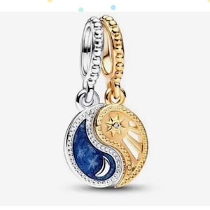 Puede incluir: Un amuleto de plata y oro en forma de símbolo yin yang. El lado yin es azul con una luna creciente y el lado yang es dorado con un sol y una estrella.