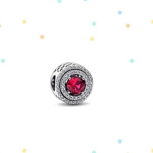 May include: A silver charm with a red gemstone surrounded by two rows of clear cubic zirconia stones.