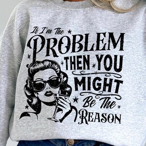 May include: Gray sweatshirt with a black graphic print of a woman with a martini glass and the text "If I'm the problem then you might be the reason".
