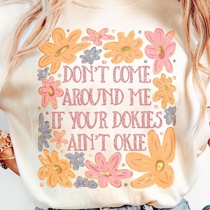 May include: A white t-shirt with a floral design and the text "Don't come around me if your cookies ain't okie".