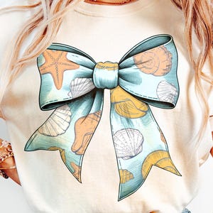 May include: A light blue bow with a seashell and starfish design. The bow is on a white t-shirt.