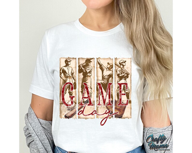 K&ouml;nnte beinhalten: Wei&szlig;es T-Shirt mit einem Baseball-Motiv. Das Design zeigt vier Baseballspieler und die Worte "GAME DAY" in einer roten, strukturierten Schriftart. Das T-Shirt hat einen klassischen Rundhalsausschnitt.