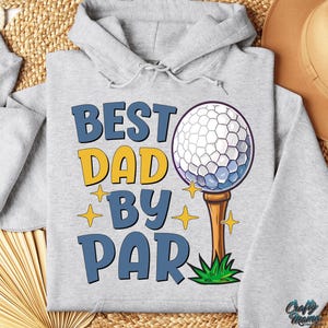 May include: A light grey hoodie featuring the text "BEST DAD BY PAR" in blue and yellow. The design includes a golf ball on a tee and star accents. The hoodie has a drawstring hood.