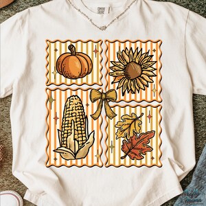 Puede incluir: Camiseta color crema con un dise&ntilde;o tem&aacute;tico de oto&ntilde;o. El dise&ntilde;o incluye una calabaza, un girasol, una mazorca de ma&iacute;z, un lazo y hojas de oto&ntilde;o, cada uno en un cuadrado con un fondo a rayas. La camiseta tiene una etiqueta Comfort Colors.