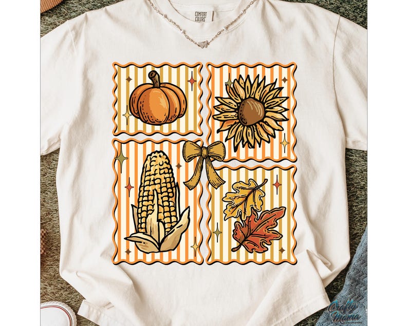 Puede incluir: Camiseta color crema con un dise&ntilde;o tem&aacute;tico de oto&ntilde;o. El dise&ntilde;o incluye una calabaza, un girasol, una mazorca de ma&iacute;z, un lazo y hojas de oto&ntilde;o, cada uno en un cuadrado con un fondo a rayas. La camiseta tiene una etiqueta Comfort Colors.