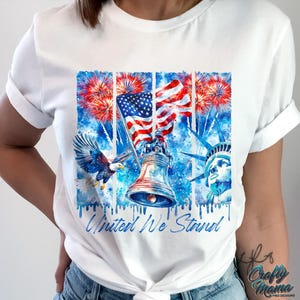 Pu&ograve; includere: Maglietta bianca con un design ad acquerello che presenta una bandiera americana, un'aquila calva, la Statua della Libert&agrave; e una campana. Il design &egrave; circondato da fuochi d'artificio e il testo "United We Stand".