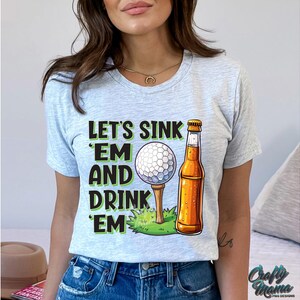 Pode incluir: T-shirt cinza claro com o texto "LET'S SINK 'EM AND DRINK 'EM" em preto e verde. Uma bola de golfe num tee e uma garrafa de cerveja s&atilde;o ilustradas. Uma pe&ccedil;a de roupa casual para o dia a dia.