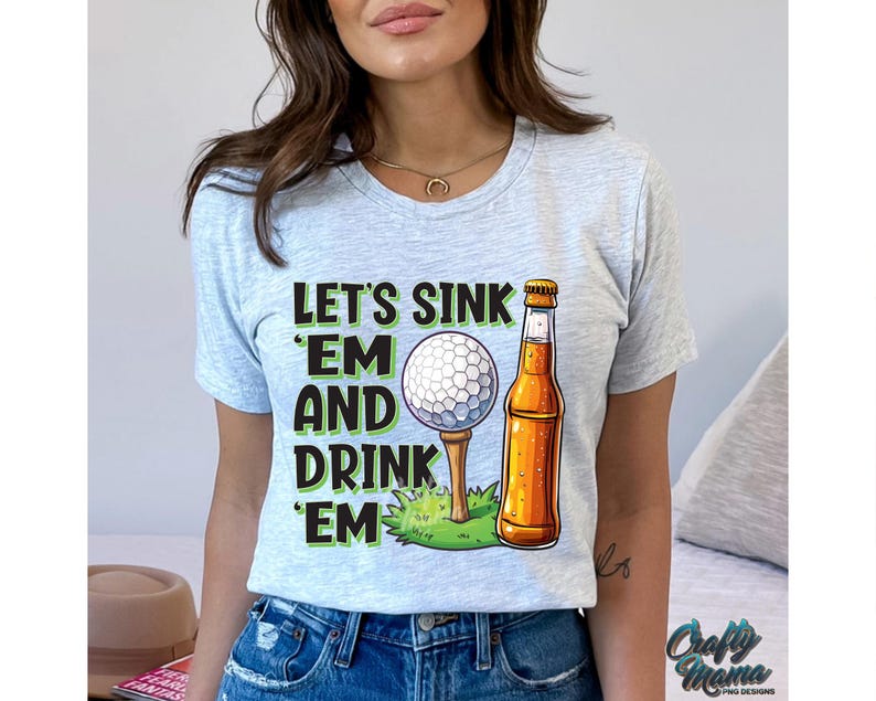 Pode incluir: T-shirt cinza claro com o texto "LET'S SINK 'EM AND DRINK 'EM" em preto e verde. Uma bola de golfe num tee e uma garrafa de cerveja s&atilde;o ilustradas. Uma pe&ccedil;a de roupa casual para o dia a dia.