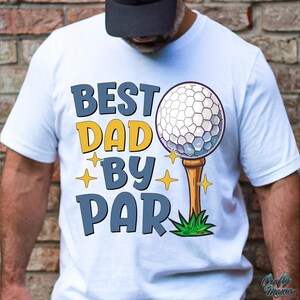 May include: White t-shirt with the text "BEST DAD BY PAR" in blue and yellow. A golf ball on a tee is featured in the design, along with star accents. The shirt is a casual style.
