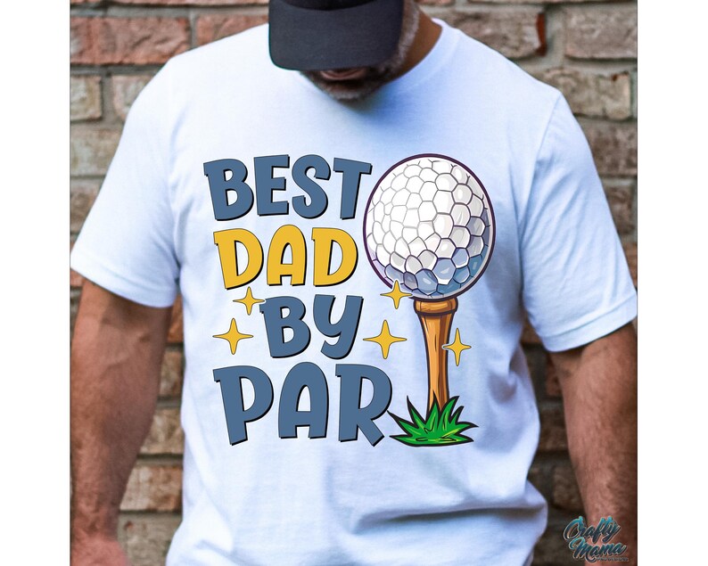 May include: White t-shirt with the text "BEST DAD BY PAR" in blue and yellow. A golf ball on a tee is featured in the design, along with star accents. The shirt is a casual style.