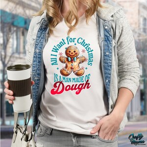 May include: White t-shirt with a gingerbread man graphic and the text "All I want for Christmas is a man made of dough." The gingerbread man has a smiling face and is wearing a bow tie. The shirt is a festive holiday design.