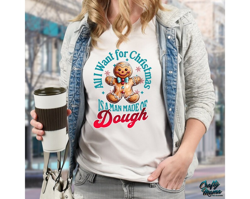 May include: White t-shirt with a gingerbread man graphic and the text "All I want for Christmas is a man made of dough." The gingerbread man has a smiling face and is wearing a bow tie. The shirt is a festive holiday design.