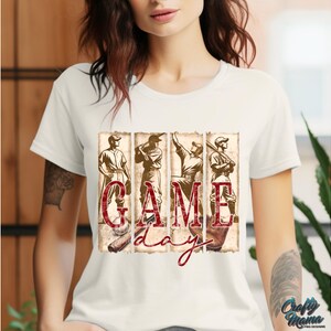 K&ouml;nnte beinhalten: Cremefarbenes T-Shirt mit Baseball-Motiv. Das Design umfasst vier Baseballspieler und die Worte "GAME DAY" in einem Used-Vintage-Stil. Die Grafik ist in Braun- und Rott&ouml;nen gehalten.