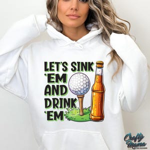 Pode incluir: Moletom branco com a frase "LET'S SINK 'EM AND DRINK 'EM" em verde e preto. O design inclui uma bola de golfe em um tee, uma garrafa de cerveja e grama verde. O logotipo "Crafty Mama" est&aacute; no canto inferior direito.
