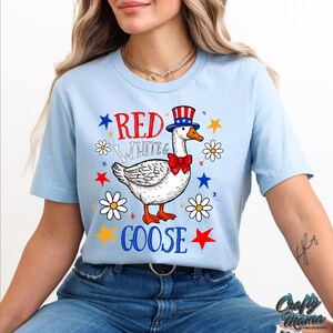 May include: A light blue t-shirt with a red, white, and blue goose wearing a red, white, and blue hat and a red bow tie. The text "Red White & Goose" is printed on the shirt.