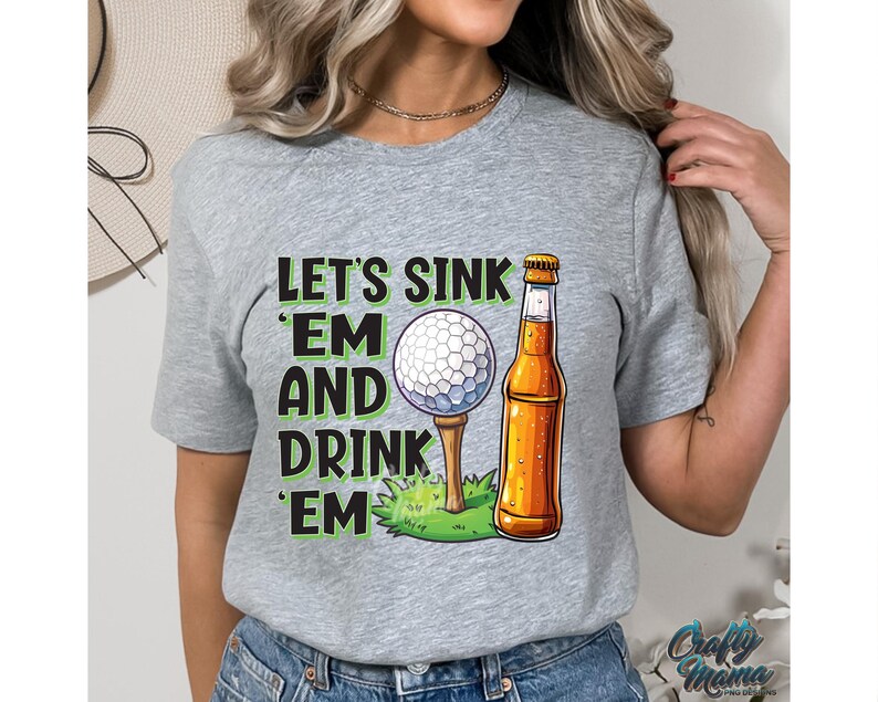 Pode incluir: Camiseta cinza com o texto "Let's Sink 'Em and Drink 'Em" em verde e preto. O design inclui uma bola de golfe em um tee e uma garrafa de cerveja. A camiseta &eacute; de estilo casual.