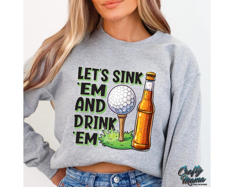 Pode incluir: Camisola cinzenta com o texto "LET'S SINK 'EM AND DRINK 'EM" em preto e verde. O gr&aacute;fico inclui uma bola de golfe num tee, uma garrafa de cerveja e relva verde. A camisola &eacute; de estilo casual.