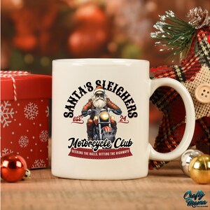 Puede incluir: Taza de cer&aacute;mica blanca con un gr&aacute;fico de Pap&aacute; Noel conduciendo una motocicleta. El texto en la taza dice "Santa's Sleighers est. 24 Motorcycle Club Decking the halls, hitting the highways".