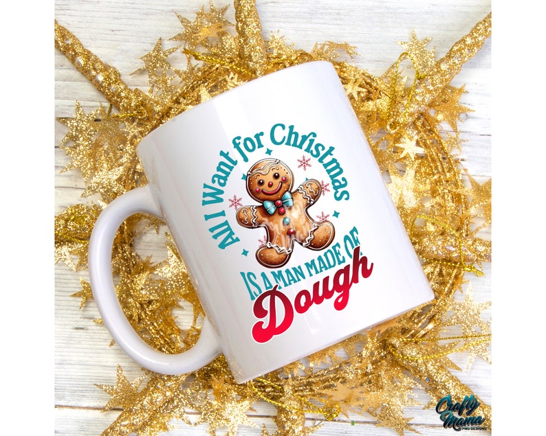 May include: White ceramic mug with a handle, featuring a gingerbread man illustration and the text "All I want for Christmas is a man made of dough" in teal and red. The mug is surrounded by gold star-shaped decorations.