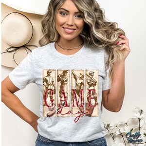 K&ouml;nnte beinhalten: Hellgraues T-Shirt mit einem Baseball-Motiv im Vintage-Stil. Das Design zeigt Baseballspieler und die Worte "GAME DAY" in roter Schrift. Das T-Shirt hat einen Rundhalsausschnitt und kurze &Auml;rmel.