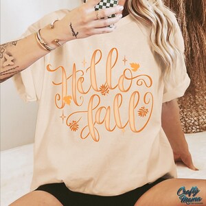 Puede incluir: Camiseta color crema con la frase "Hello Fall" en escritura naranja. El dise&ntilde;o incluye hojas y estrellas naranjas. Es una prenda de vestir casual y de temporada.