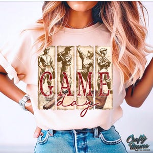 K&ouml;nnte beinhalten: Cremefarbenes T-Shirt mit Baseball-Motiv. Das Design umfasst Illustrationen von Baseballspielern im Vintage-Stil und die Worte "GAME day" in einer Used-Schrift. Das Shirt hat kurze &Auml;rmel und einen Rundhalsausschnitt.