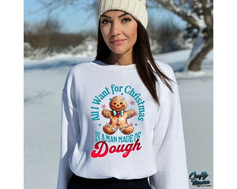 May include: White sweatshirt with a gingerbread man graphic and the text "All I want for Christmas is a man made of Dough". The gingerbread man has a blue bow tie and is surrounded by teal text and red text.