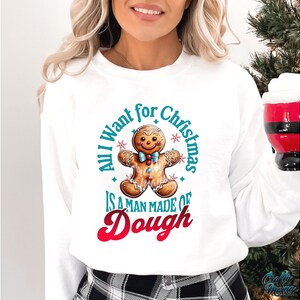 May include: White sweatshirt with a gingerbread man graphic and the text "All I want for Christmas is a man made of dough." The gingerbread man has a blue bow tie and is surrounded by blue stars.