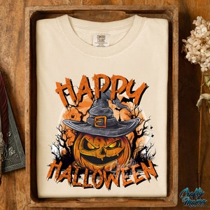 Peut inclure: Un t-shirt cr&egrave;me avec un motif de citrouille portant un chapeau de sorci&egrave;re et le texte "Happy Halloween".