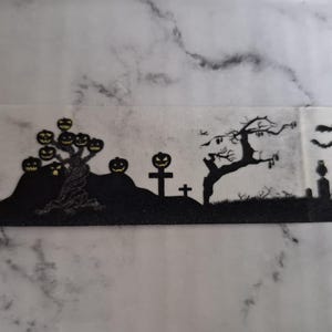 Puede incluir: Silueta negra de una escena de Halloween con un árbol con caras de calabaza, lápidas, un árbol desnudo y murciélagos volando. El diseño está sobre un fondo gris nublado, creando una atmósfera espeluznante.