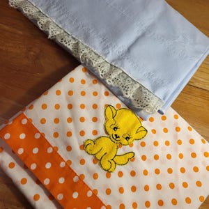 May include: Two fabric squares, one light blue with white lace trim and one white with orange polka dots and a yellow embroidered kitten.