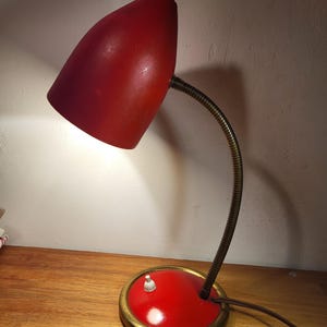May include: A red vintage desk lamp with a flexible arm and a gold base. The lampshade is a rounded cone shape.