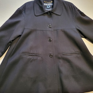 Könnte beinhalten: Schwarze Escada-Jacke mit Kragen, drei Knöpfen und zwei Vordertaschen. Die Jacke hat ein klassisches Design und ist aus glattem Stoff gefertigt. Das Escada-Logo ist in der Nähe des Kragens sichtbar.