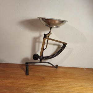 May include: A vintage silver and brass kitchen scale with a round bowl and a circular dial with markings. The scale is on a wooden surface.