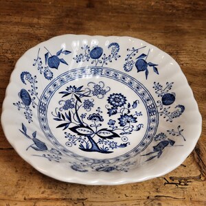 Op de afbeelding: Een witte keramische kom met een blauw bloemenpatroon. De kom heeft een gegolfde rand en is versierd met een herhalend patroon van bloemen en bladeren.