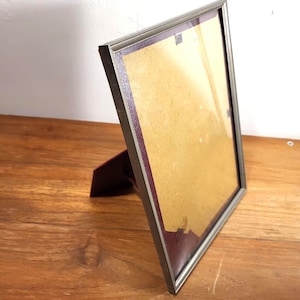May include: A silver-coloured picture frame with a burgundy mount and backing, standing on a wooden surface. The rectangular frame has a simple design. The frame is empty, ready to display a photograph or artwork.