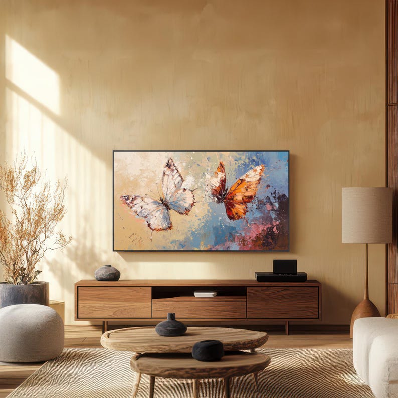 Op de afbeelding: Een woonkamer met een groot, ingelijst kunstwerk met twee vlinders met witte en oranje vleugels. Het kunstwerk hangt boven een houten tv-meubel. Een ronde salontafel en een vloerlamp zijn ook zichtbaar.
