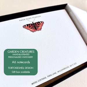 May include: A white A6 notecard featuring a hand-illustrated orange and black tortoiseshell butterfly. The text HANA OLIVE PEARSON is printed above the butterfly. The text MOSS COTTAGE, FERN LANE, WILLOWBROOK, AB12 3CD is printed at the bottom right.