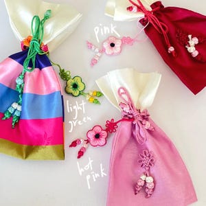 Pu&ograve; includere: Quattro sacchetti di raso colorati con accenti floreali decorativi. I sacchetti sono in tonalit&agrave; di rosa, rosso e blu, con la parte superiore bianca. L'immagine include il testo "pink", "light green" e "hot pink".