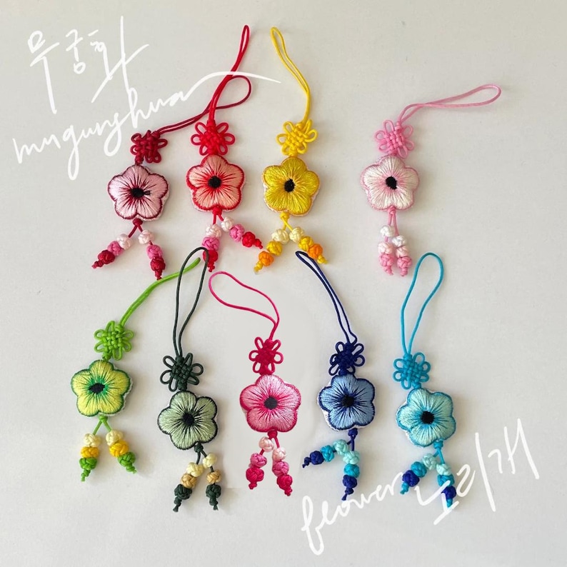 Pu&ograve; includere: Una collezione di ornamenti floreali fatti a mano in vari colori, tra cui rosa, rosso, giallo, verde e blu. Ogni ornamento presenta un design floreale con ricami intricati e dettagli di perline. Il testo coreano &egrave; incluso.